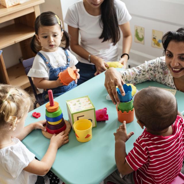 Teacher smiling and helping nursey school children.