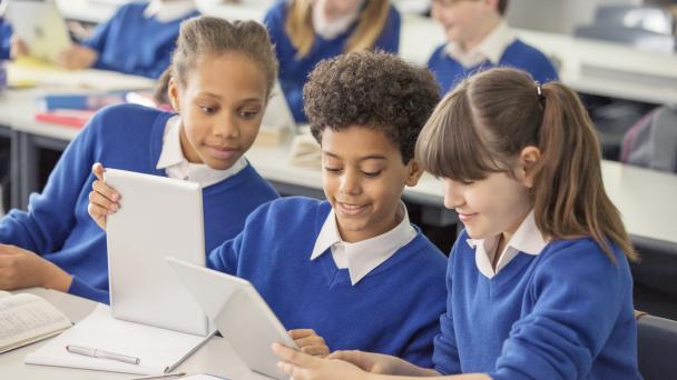 Pupils wearing blue uniforms working together collaboratively on smart screens. 